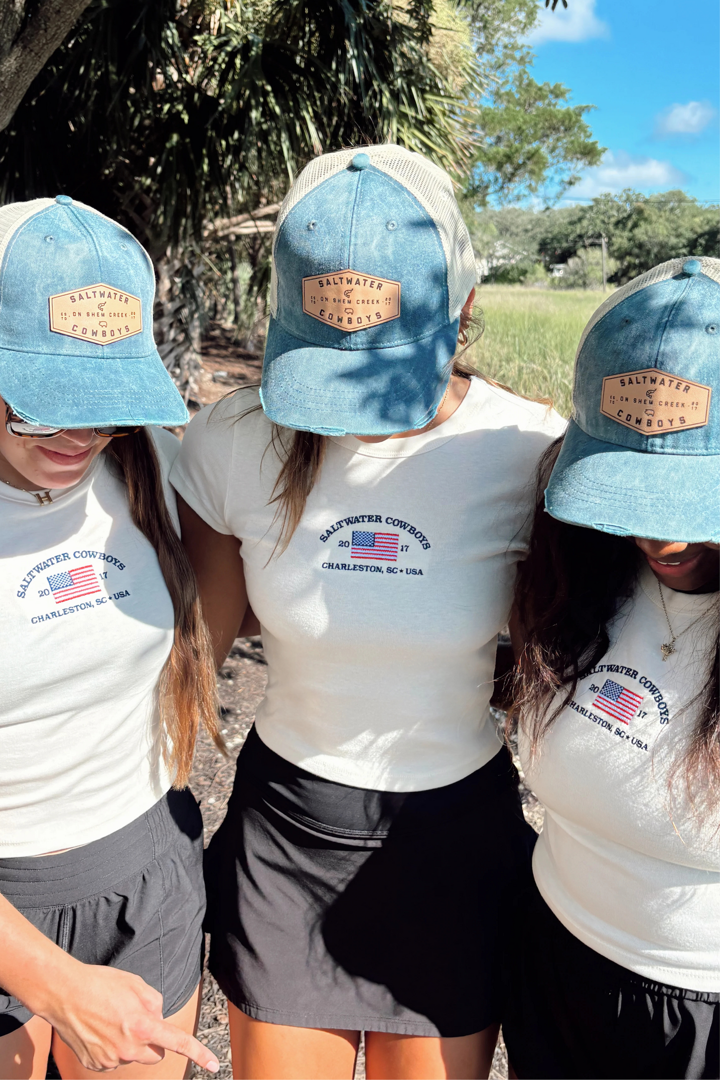 Three people wearing matching blue caps and white shirts with a logo in an outdoor setting.